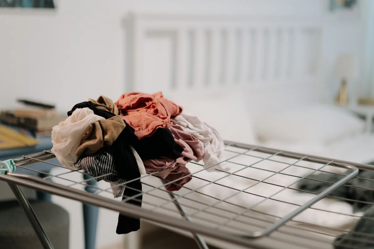 Ropa de varios colores sobre un tendedero plegable en un dormitorio con luz natural