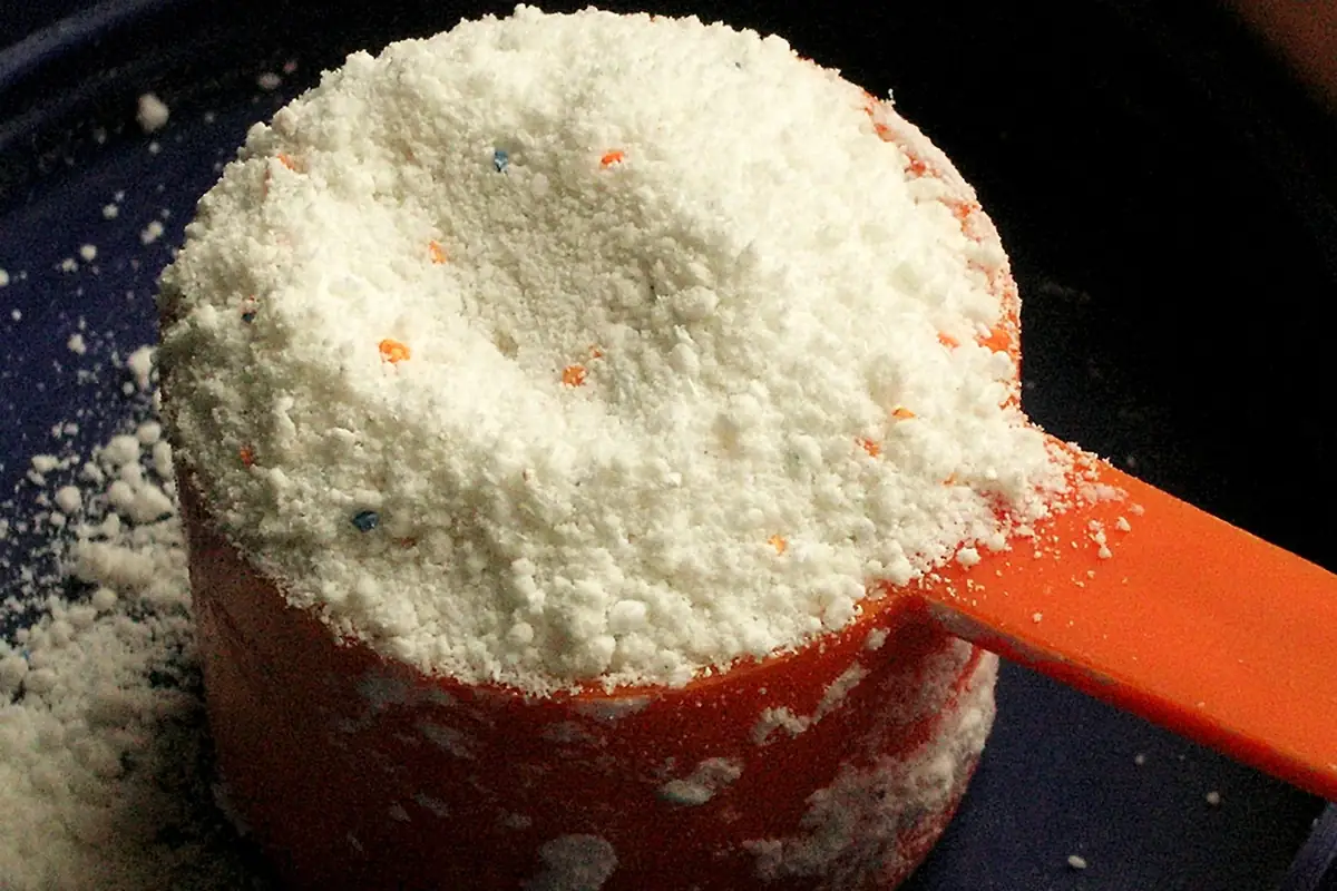 Medidor naranja colmado de detergente en polvo sobre un fondo azul oscuro