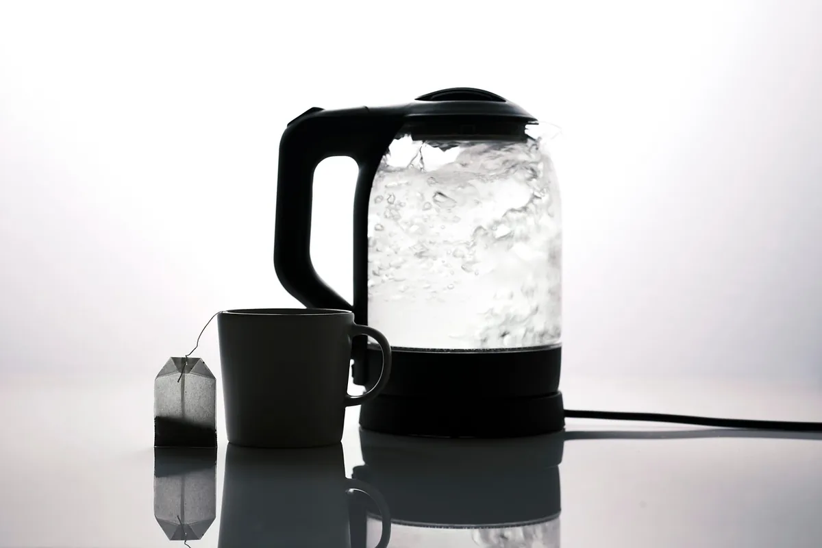 Hervidor eléctrico de cristal con agua hirviendo junto a una taza